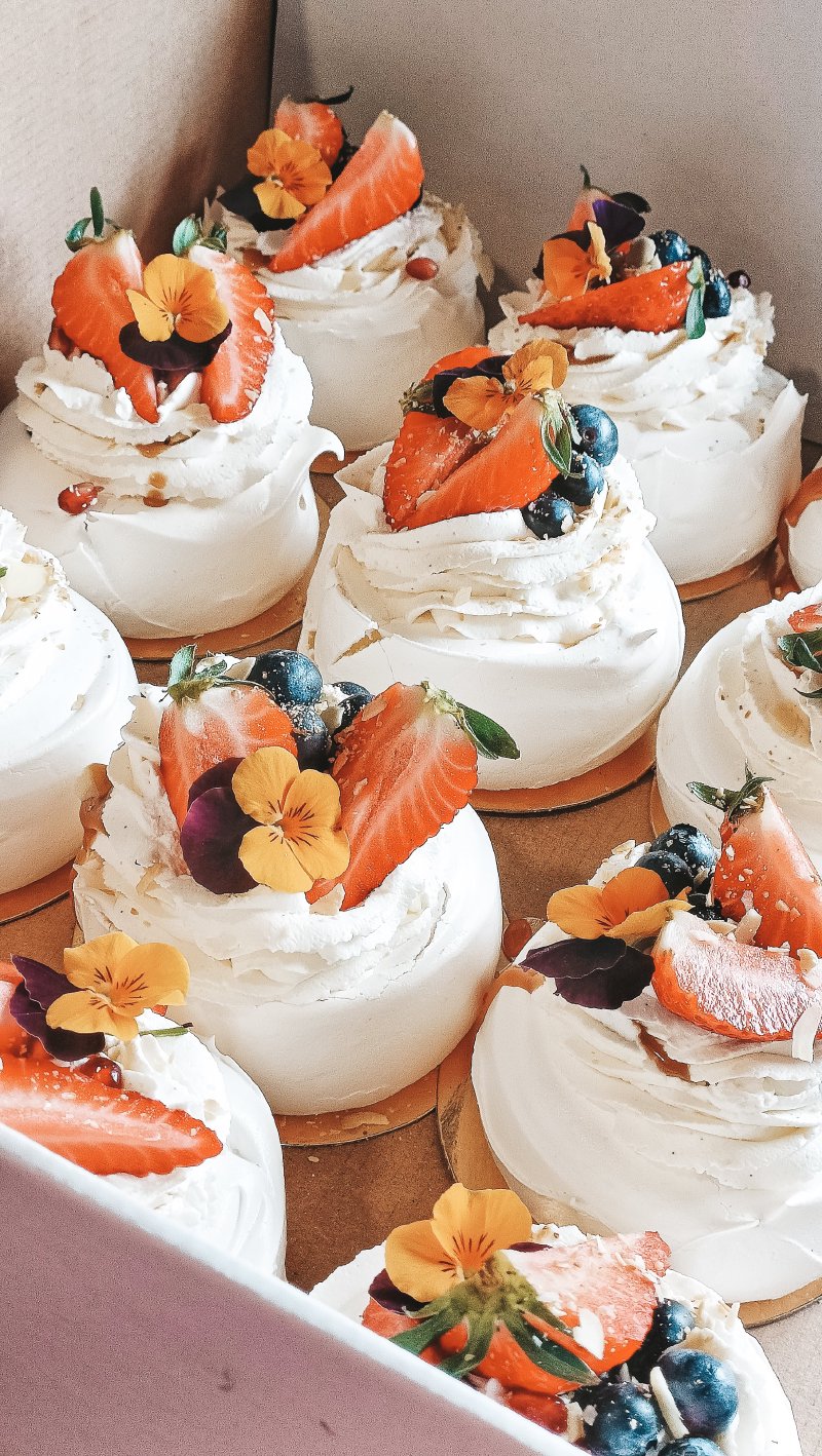 Kilka mini bez Pavlova udekorowanych śmietaną, truskawkami i jadalnymi kwiatami.