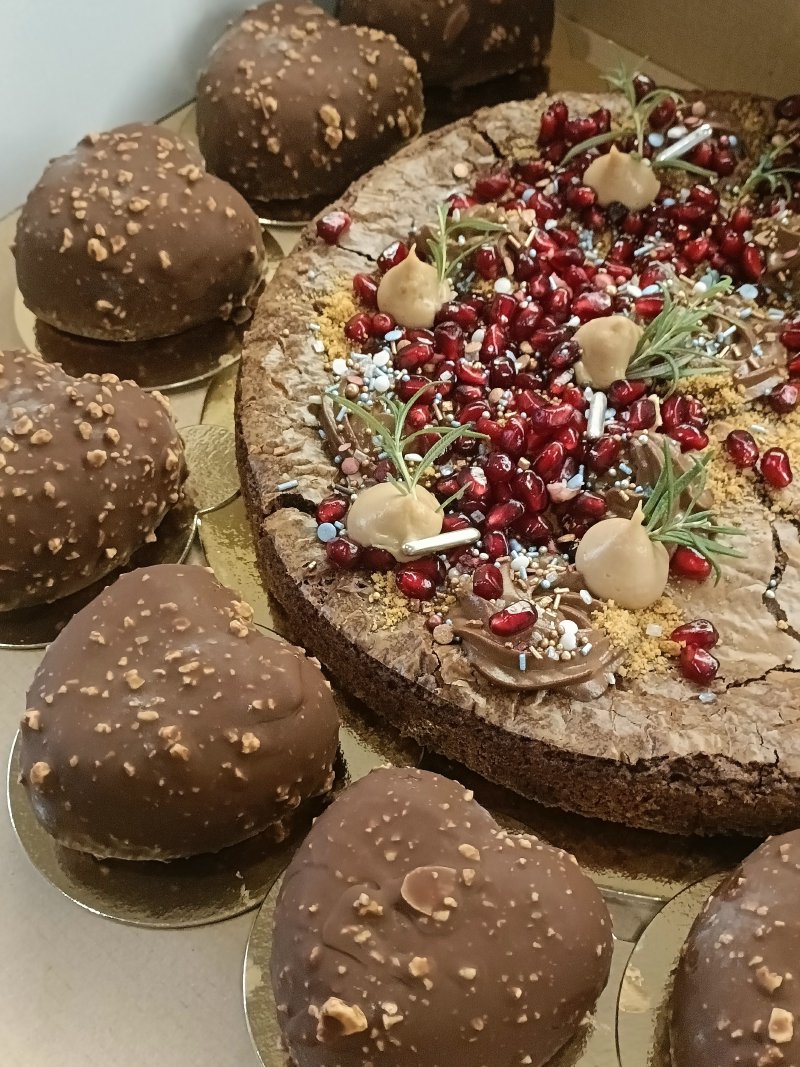 Ciasto brownie bogato udekorowane granatem i otoczone czekoladowymi pralinami.