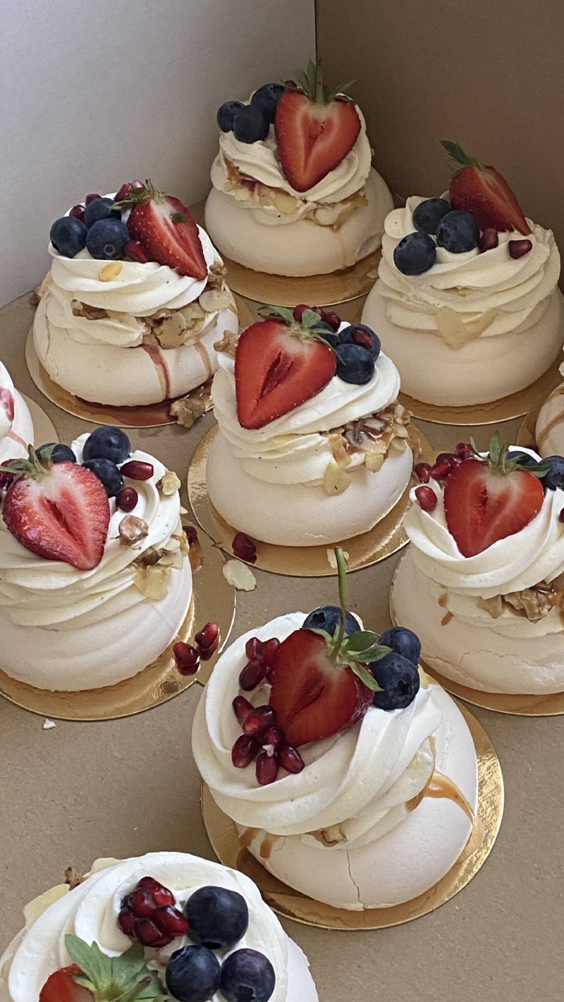 Zestaw mini bez Pavlova udekorowanych bitą śmietaną i świeżymi owocami.