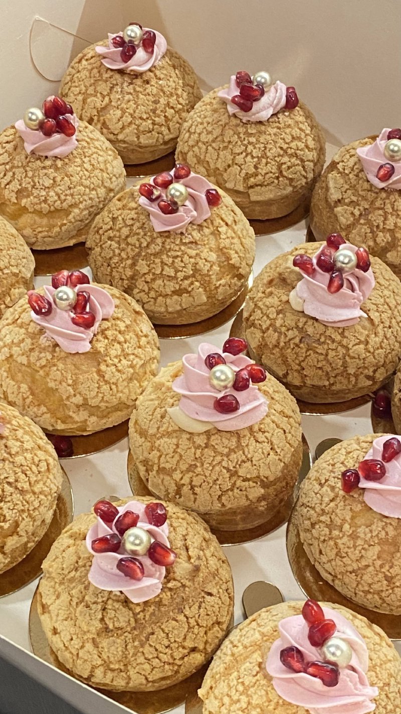 Zestaw ptysiów ze strzelistą skórką, udekorowany różowym kremem i granatem