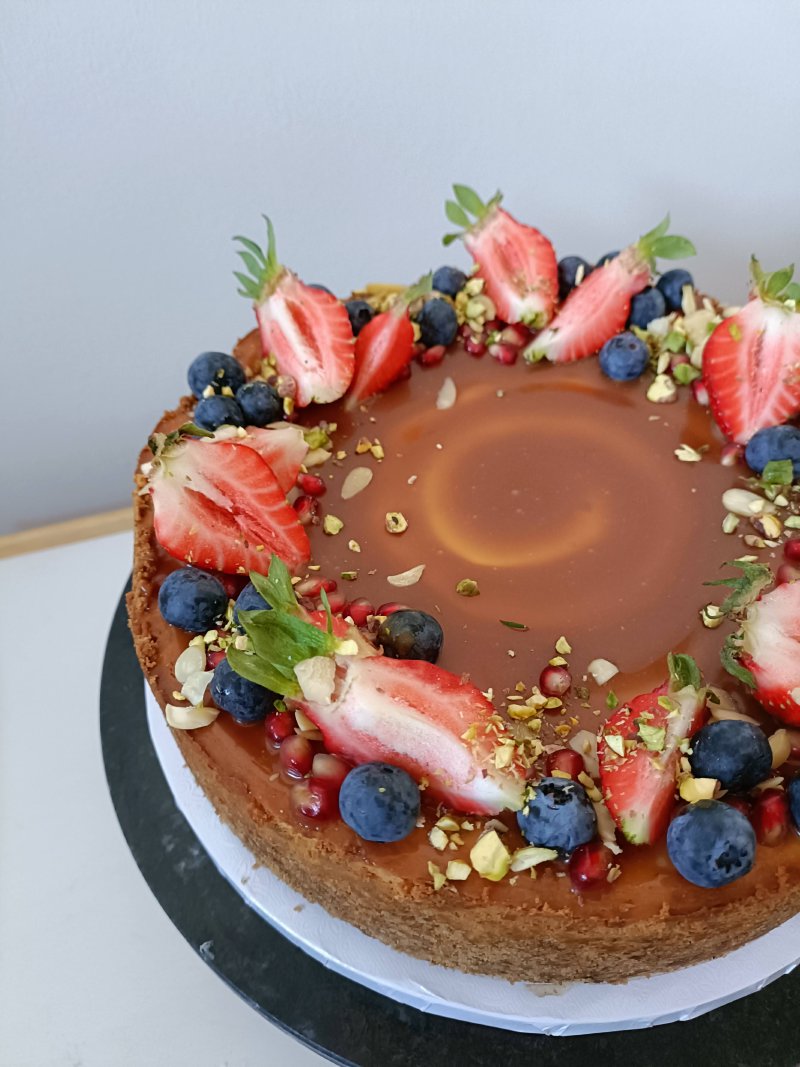 Tort karmelowy udekorowany świeżymi owocami i pistacjami.