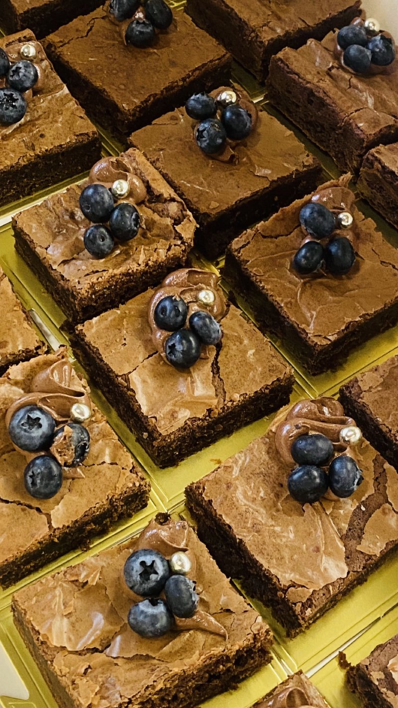 Kwadratowe porcje brownie udekorowane borówkami i kremem