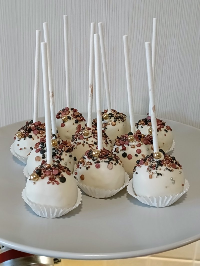 Zestaw cake popsów oblanych białą czekoladą i posypanych złotymi i brązowymi dekoracjami