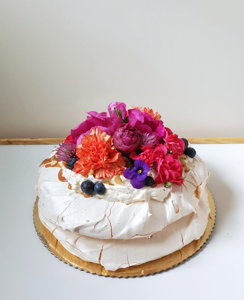 Elegancka beza Pavlova udekorowana intensywnie kolorowymi kwiatami i borówkami.