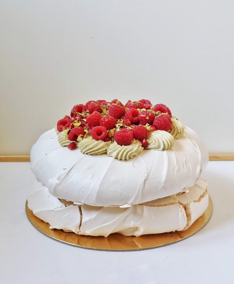 Dwuwarstwowa beza Pavlova udekorowana malinami i zielonym kremem pistacjowym.