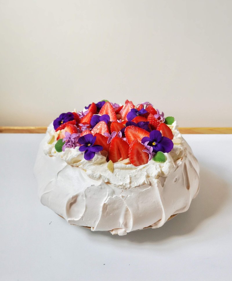 Elegancka beza Pavlova udekorowana truskawkami i fioletowymi kwiatami fiołka.
