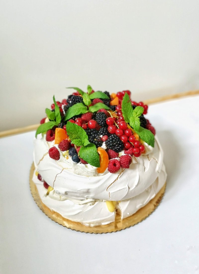 Dwuwarstwowa beza Pavlova obficie udekorowana mieszanką jagód, malin i mięty.