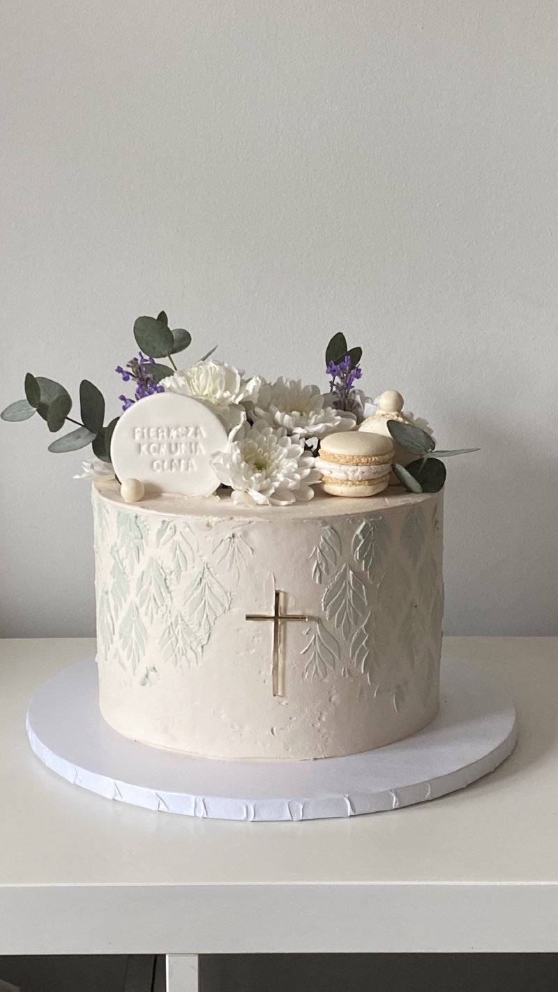 Elegancki tort komunijny z białymi kwiatami i złotym krzyżem.