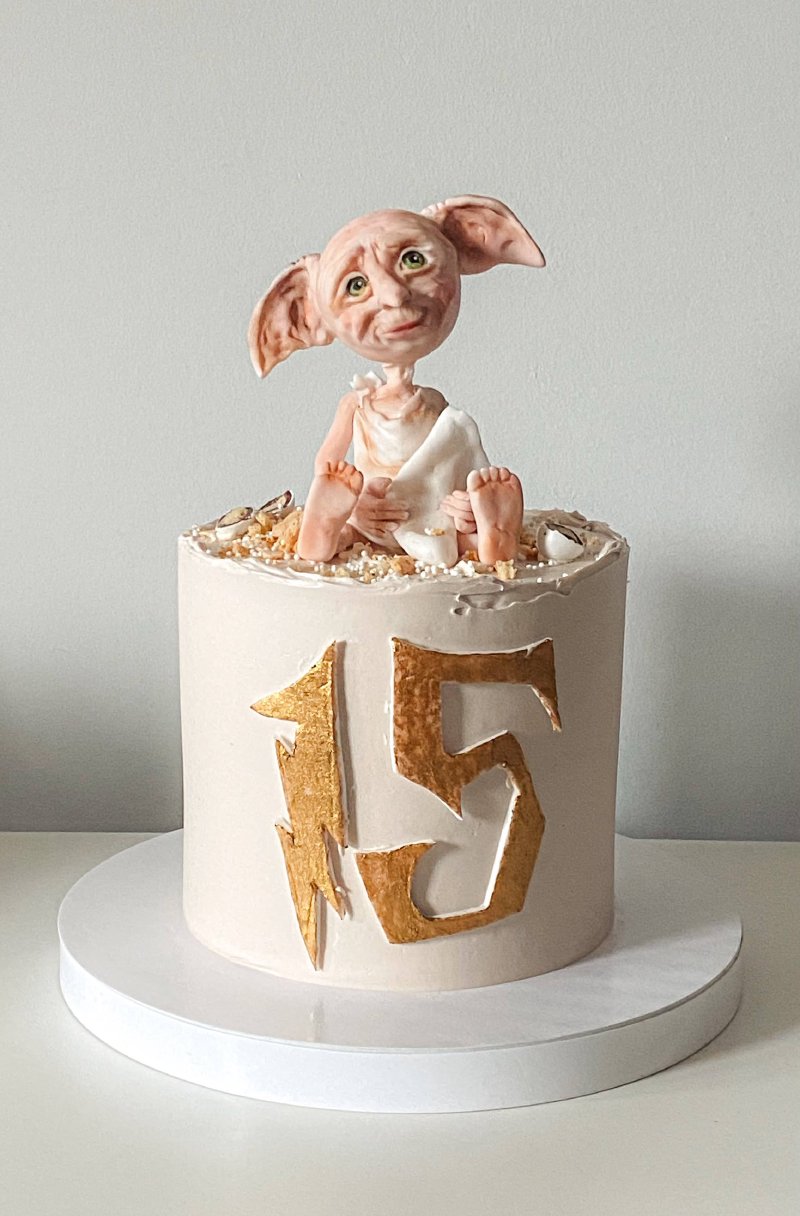 Biały tort urodzinowy z figurką Dobby'ego i złotymi liczbami 15