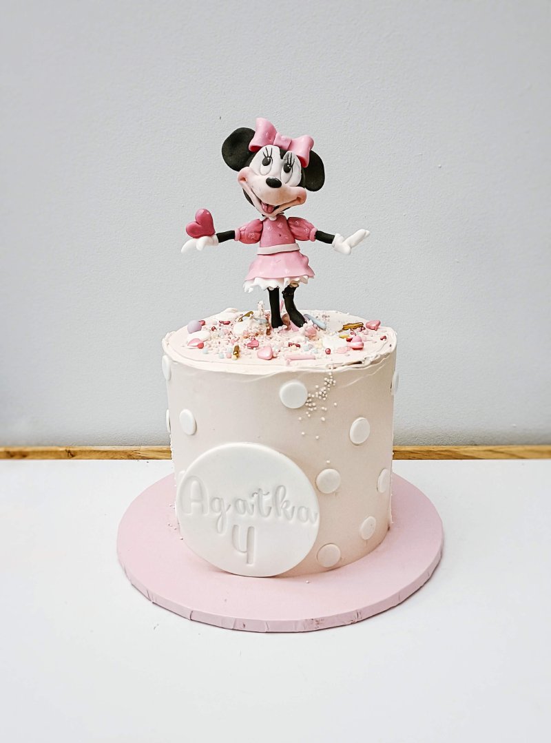 Różowy tort urodzinowy z figurką Minnie Mouse i personalizowaną tabliczką z imieniem.