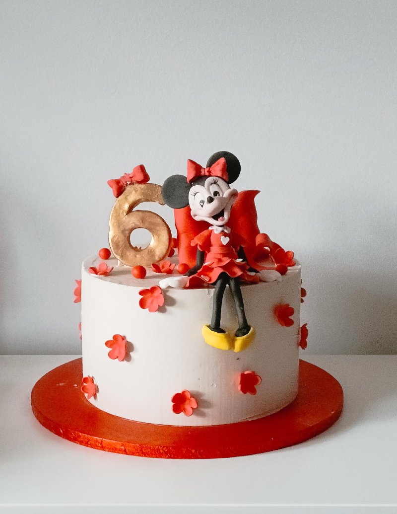 Biały tort urodzinowy z figurką Minnie Mouse i złotą cyfrą 6.