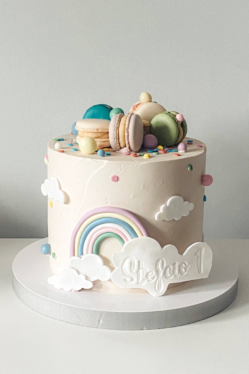 Wysoki tort urodzinowy z masą cukrową w pastelowych kształtach tęczy i chmurek.
