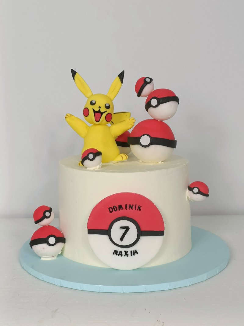 Biały tort urodzinowy z figurką Pikachu i dekoracjami Pokeball na roczek chłopca