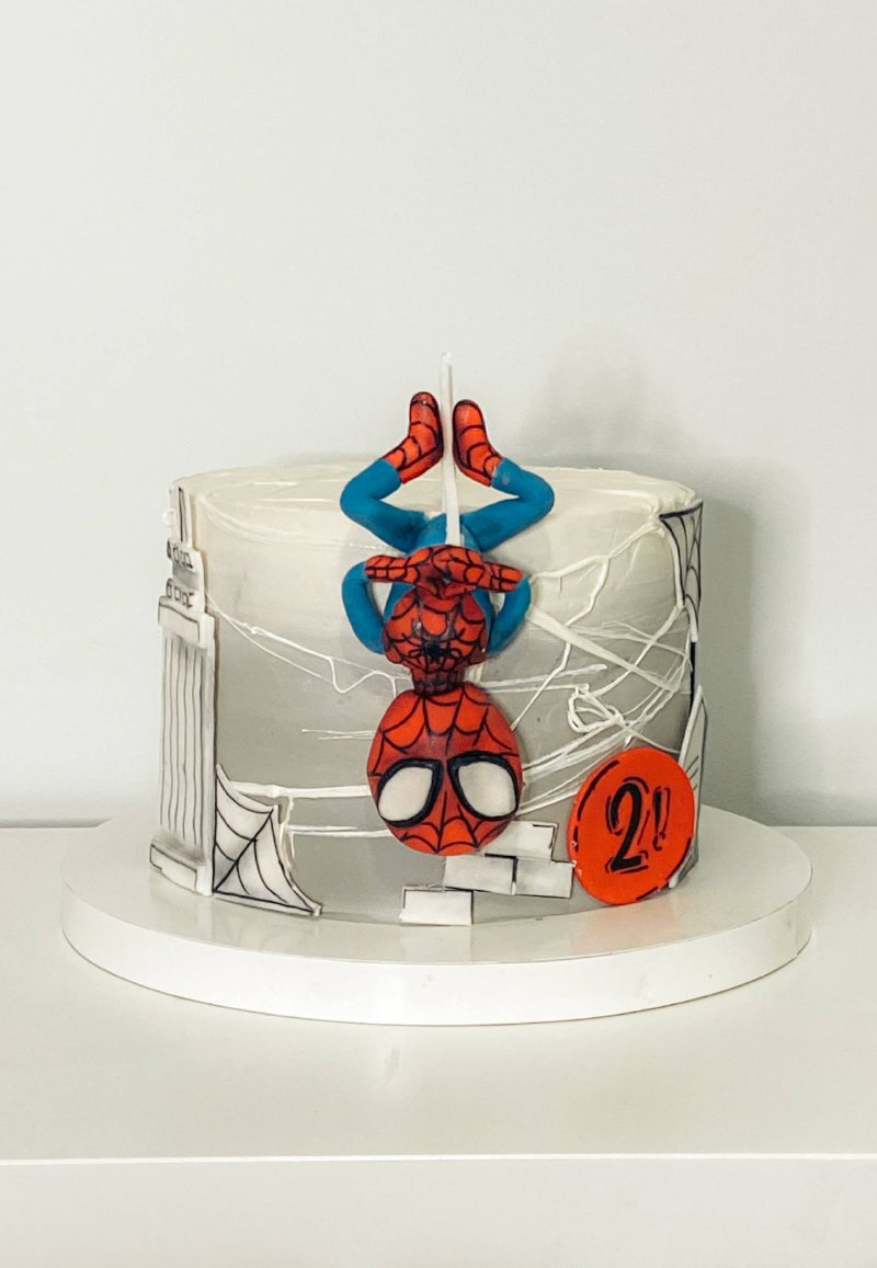 Tort urodzinowy z figurką Spidermana zwisającego głową w dół i dekoracjami imitującymi panoramę miasta.