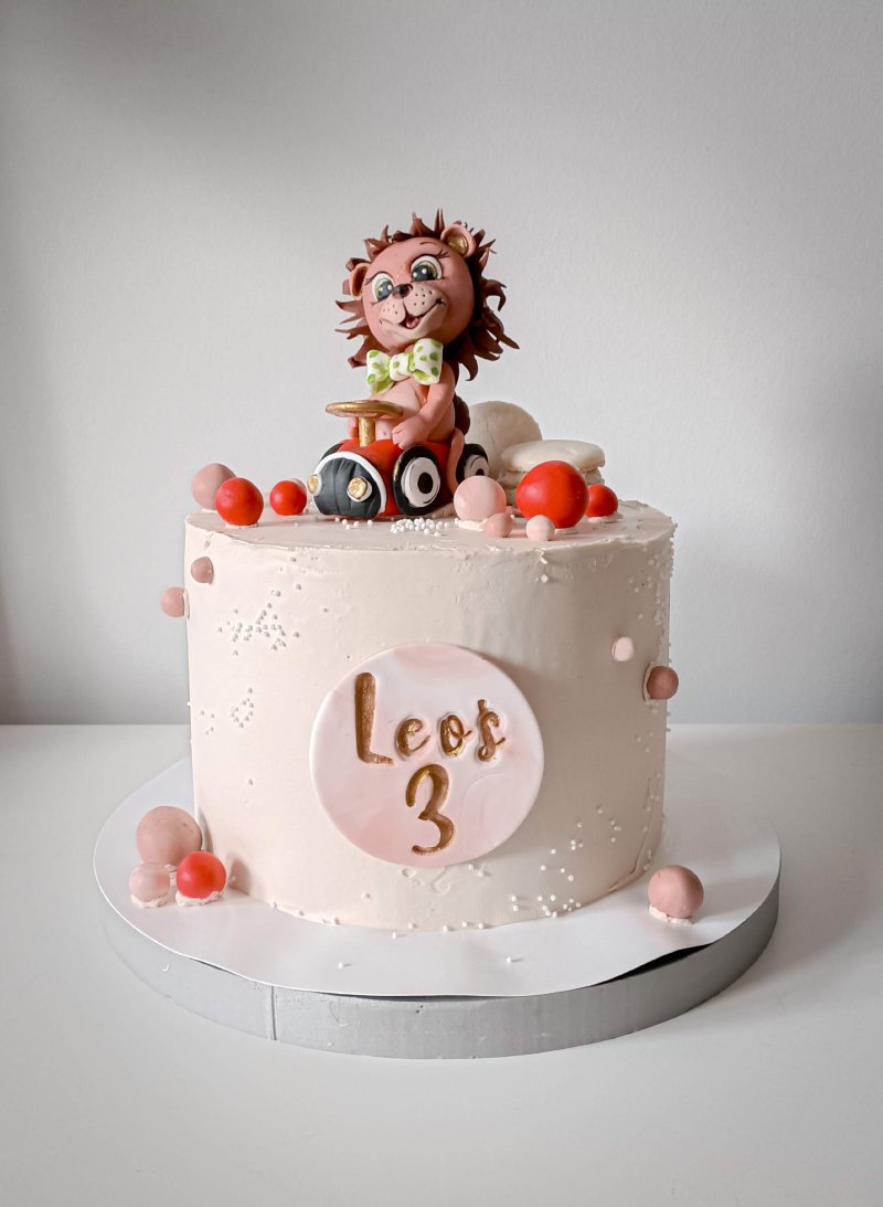 Różowy tort urodzinowy z figurką lwa na traktorze i personalizowanym napisem.