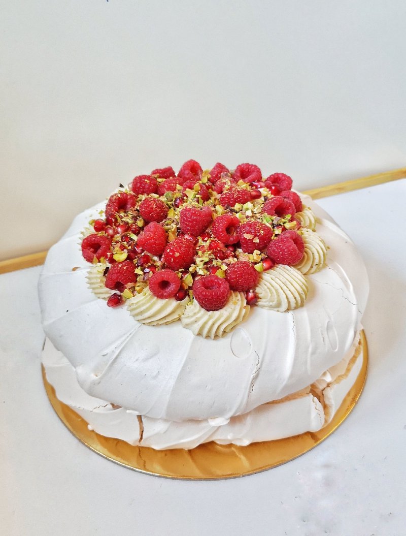 Duża beza Pavlova udekorowana świeżymi malinami i pistacjami