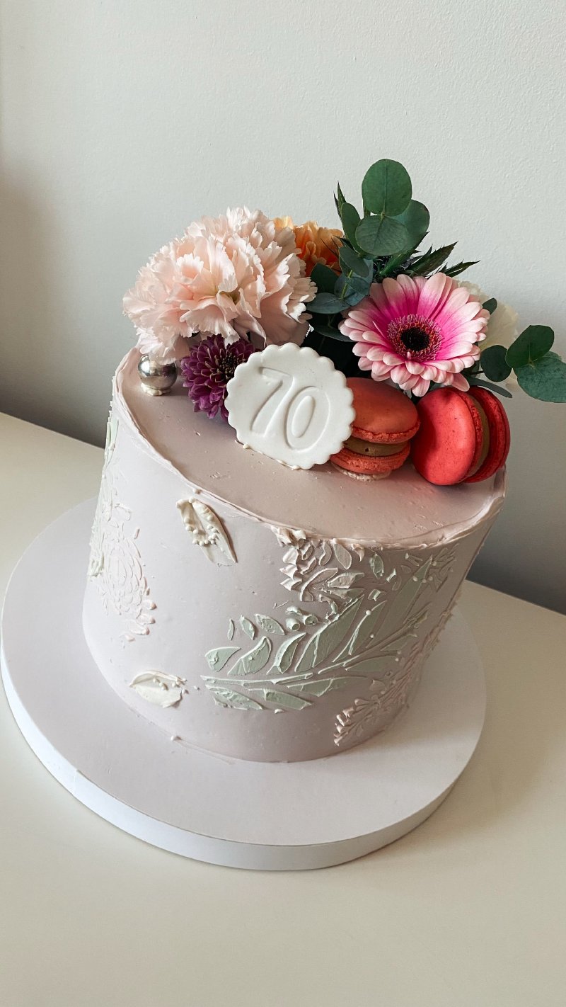 Elegancki tort urodzinowy w jasnym odcieniu z dekoracją florystyczną i numerem 70.
