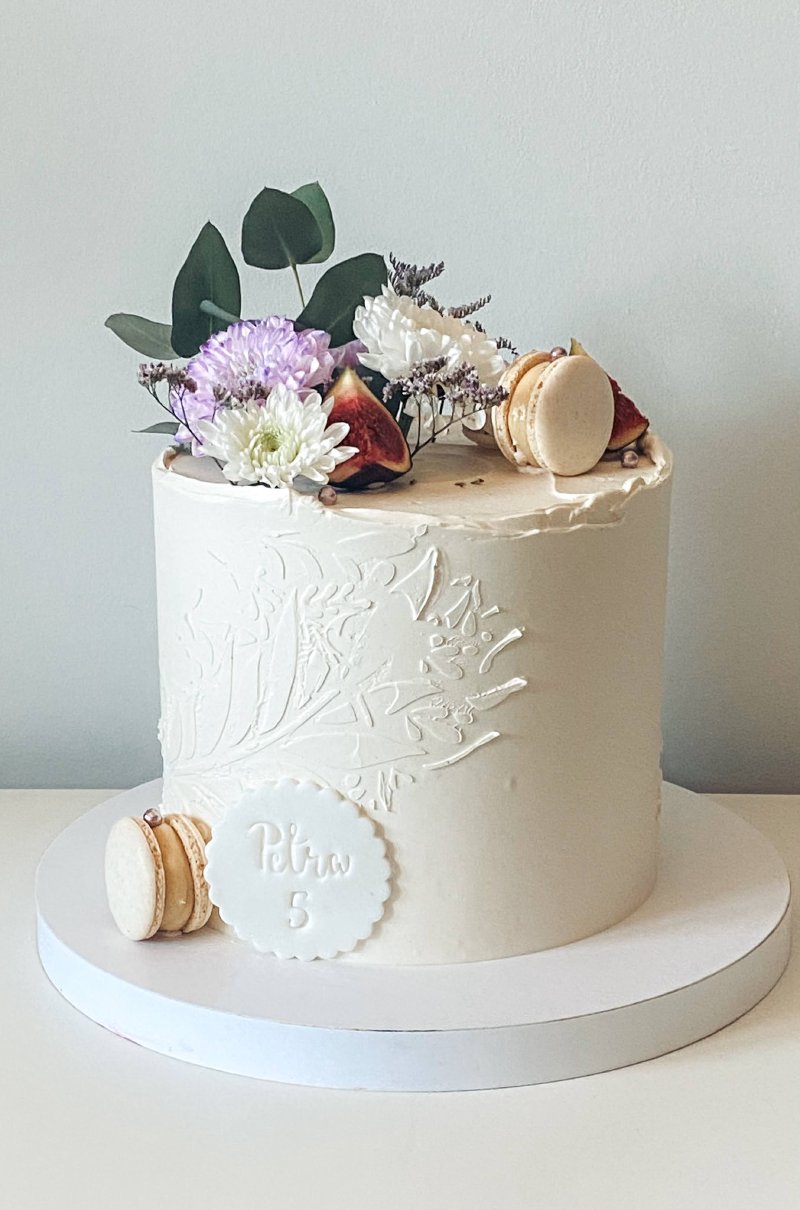 Elegancki tort na bazie kremu z dekoracją z kwiatów, makaroników i fig.