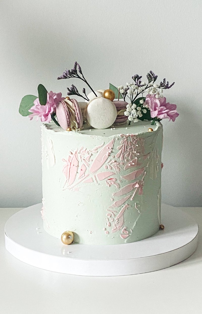Elegancki tort z różowo-miętowymi zdobieniami i dekoracją z makaroników oraz kwiatów.