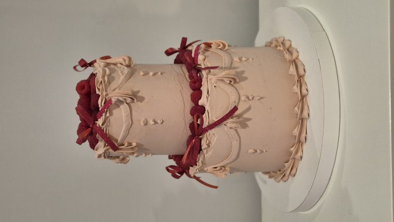Elegancki, dwupoziomowy tort w beżowym kremie z burgundowymi wstążkami.