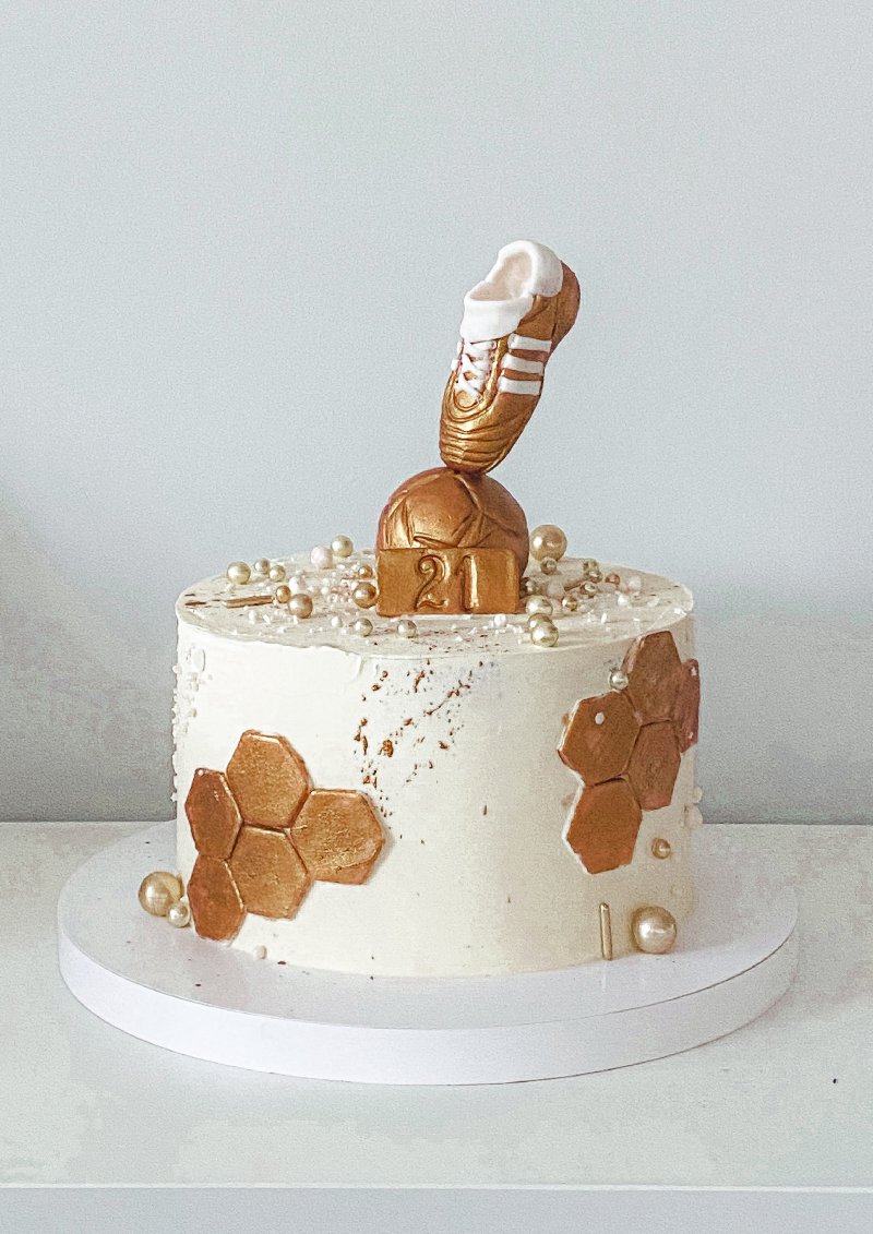 Elegancki tort urodzinowy w bieli ze złotymi akcentami i motywem piłkarskim.