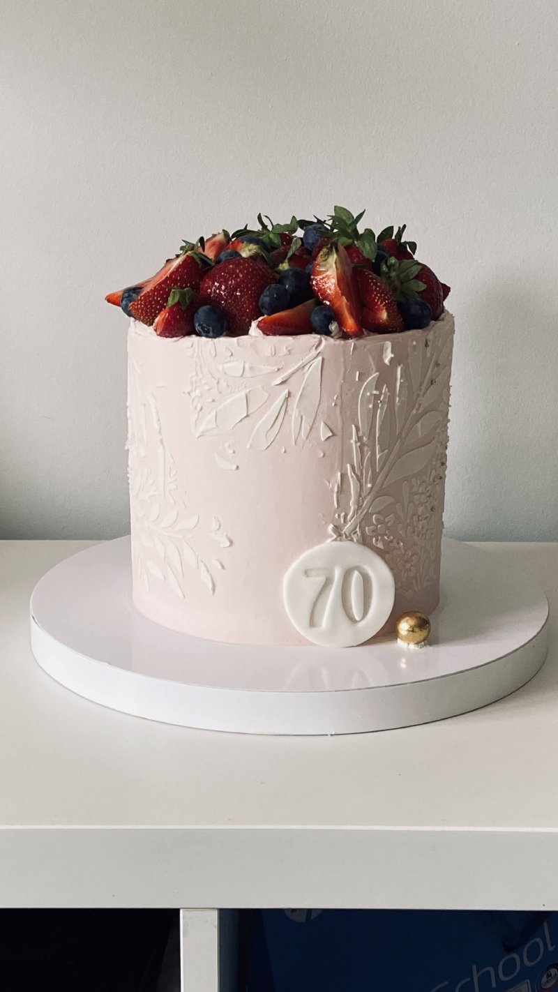 Elegancki tort urodzinowy w jasnoróżowym kolorze z reliefowym zdobieniem i koroną ze świeżych owoców.