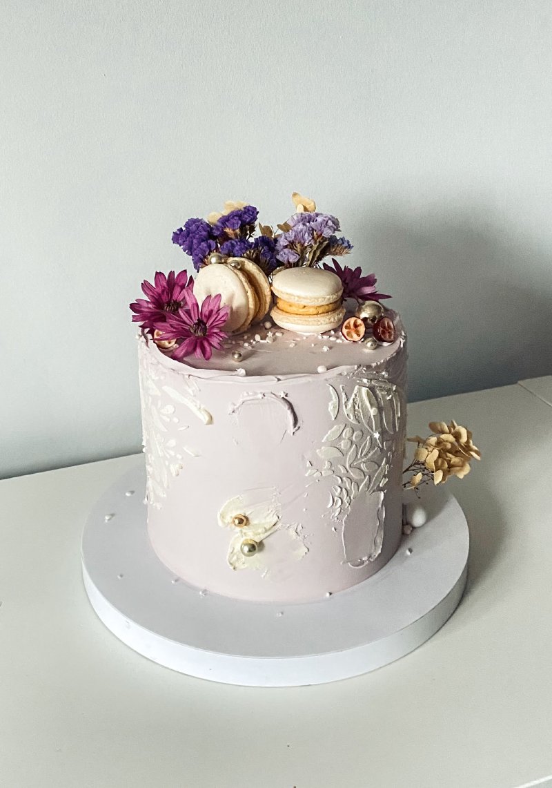 Elegancki tort pokryty lawendowym kremem, zwieńczony różowymi kwiatami i makaronikami.
