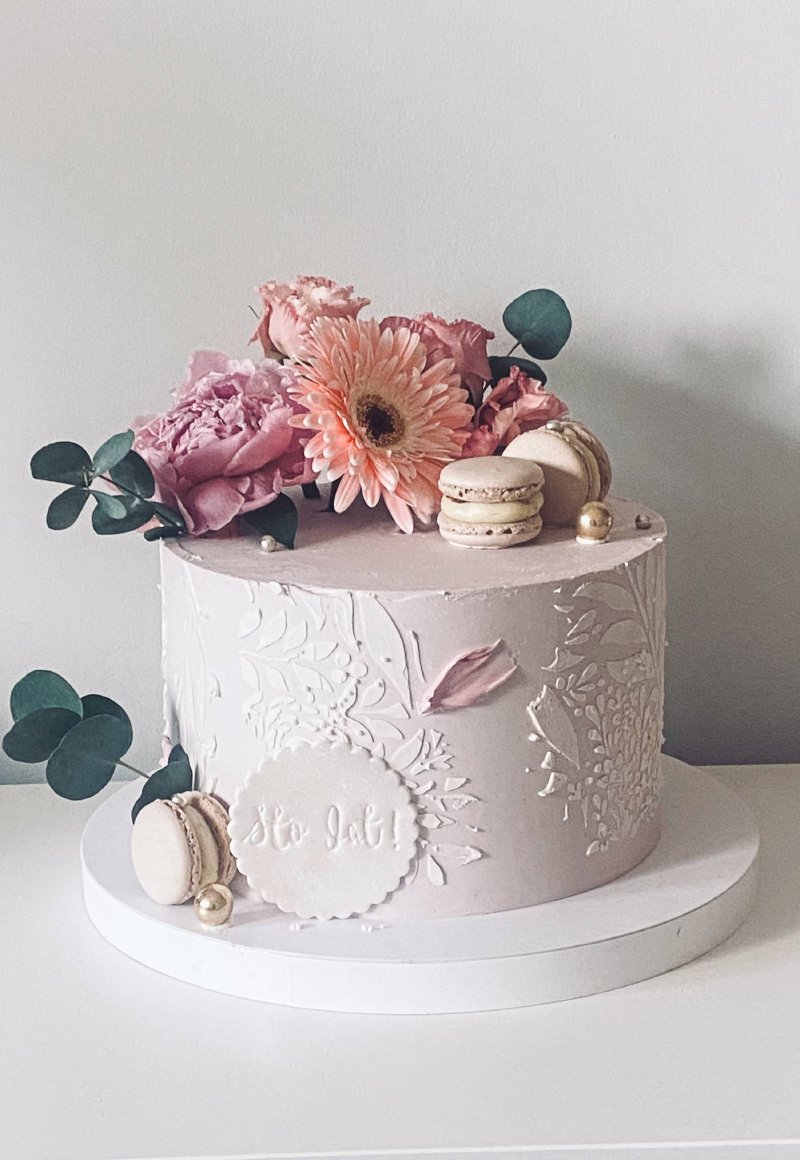 Elegancki tort kremowy z reliefem, udekorowany różowymi kwiatami i makaronikami.