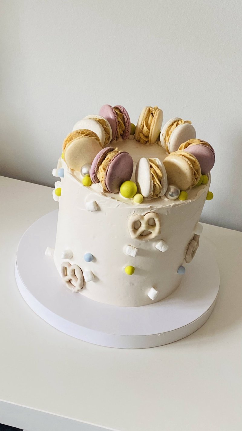 Elegancki tort oblany białą masą, zwieńczony makaronikami i drobnymi słodyczami.