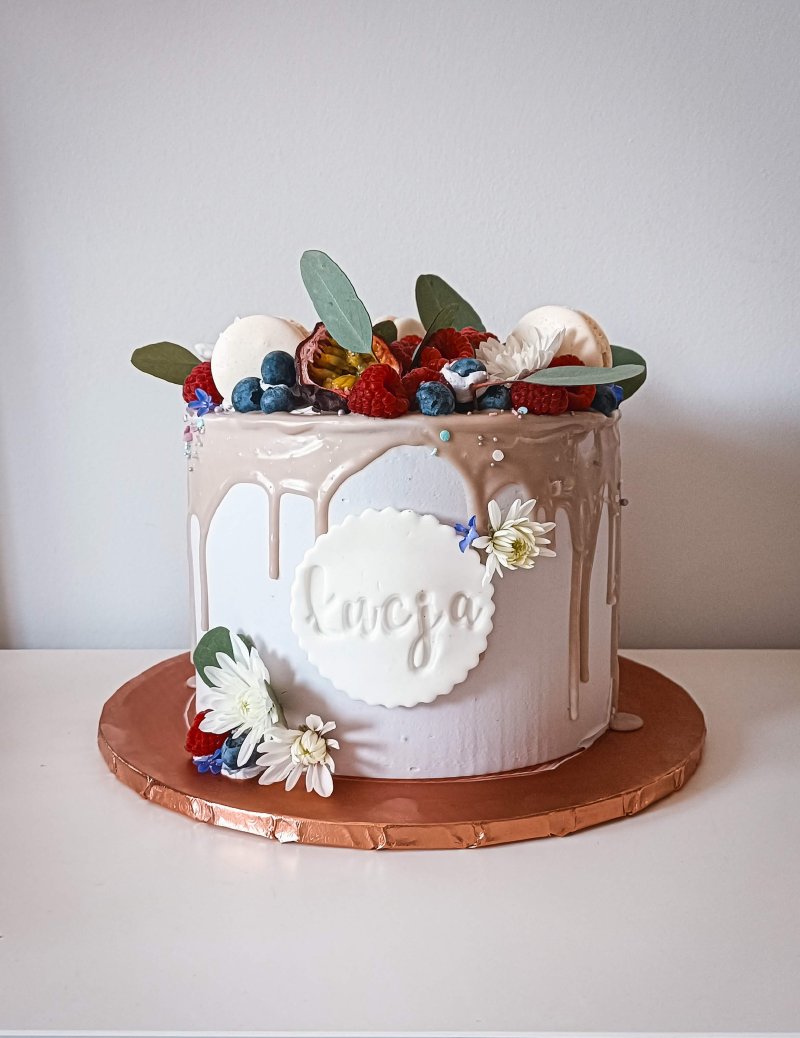 Elegancki tort personalizowany imieniem 'Łucja' z polewą drip i dekoracją z owoców i kwiatów.