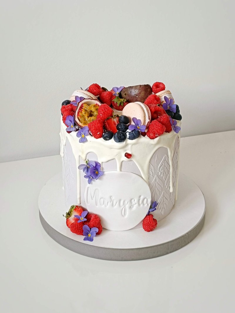 Elegancki tort z białą polewą, zdobiony świeżymi owocami i personalizowanym napisem 'Marysia'.