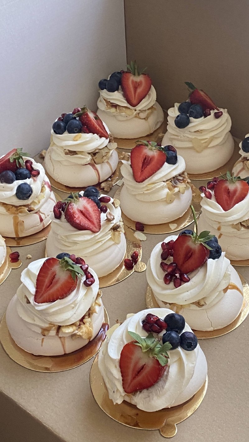 Kolekcja miniaturowych bez Pavlova udekorowanych śmietaną i świeżymi owocami.