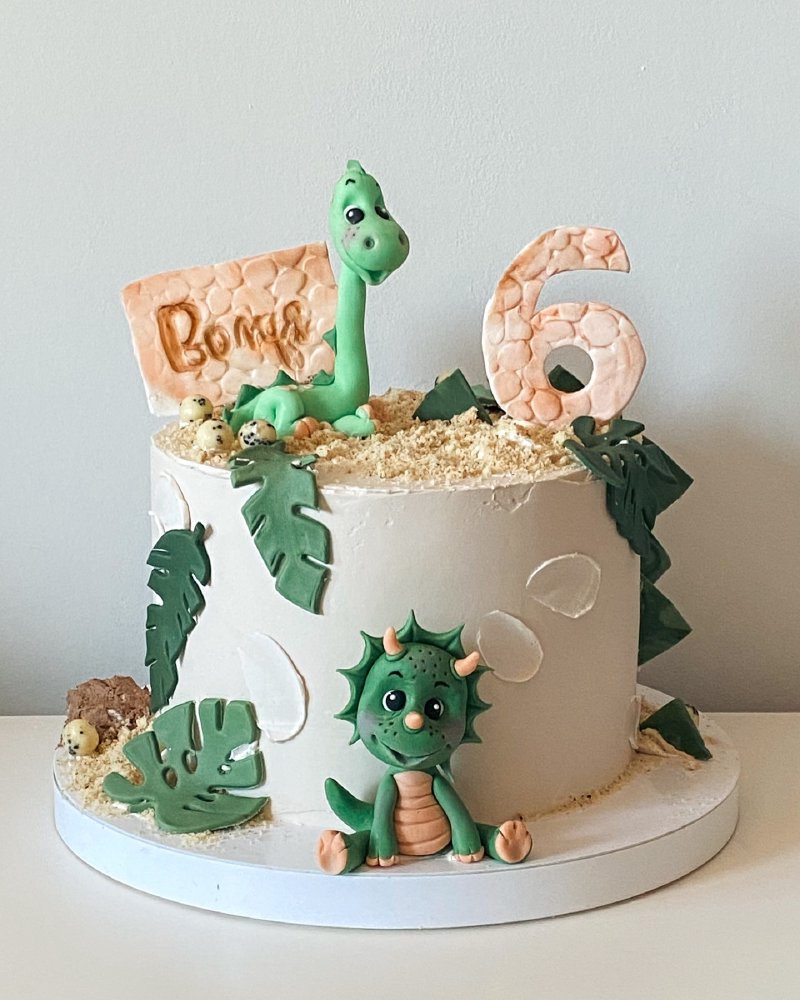 Biały tort urodzinowy dla chłopca z figurkami dinozaurów i numerem 6.