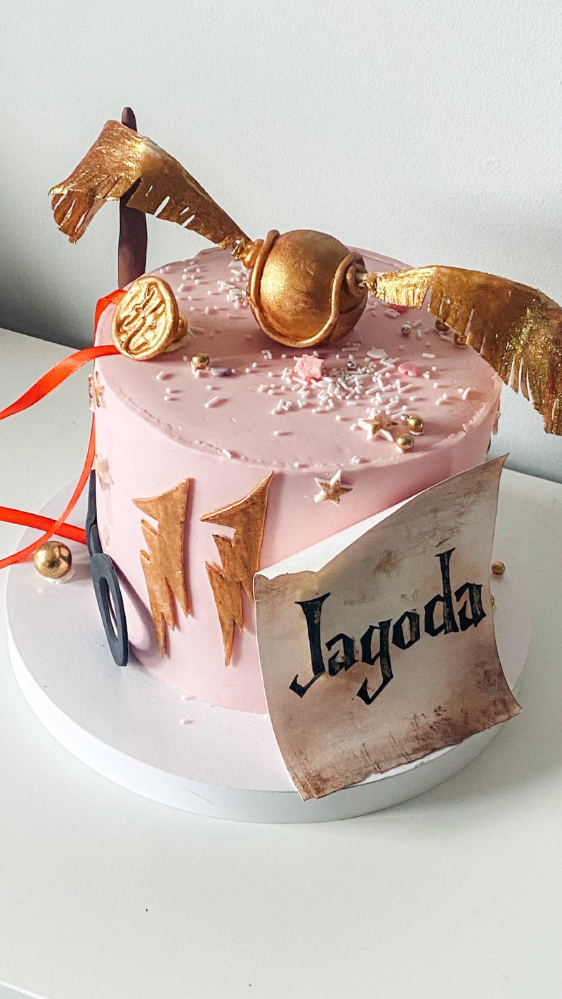 Różowy tort urodzinowy z dekoracją Znicza i personalizowaną etykietą.