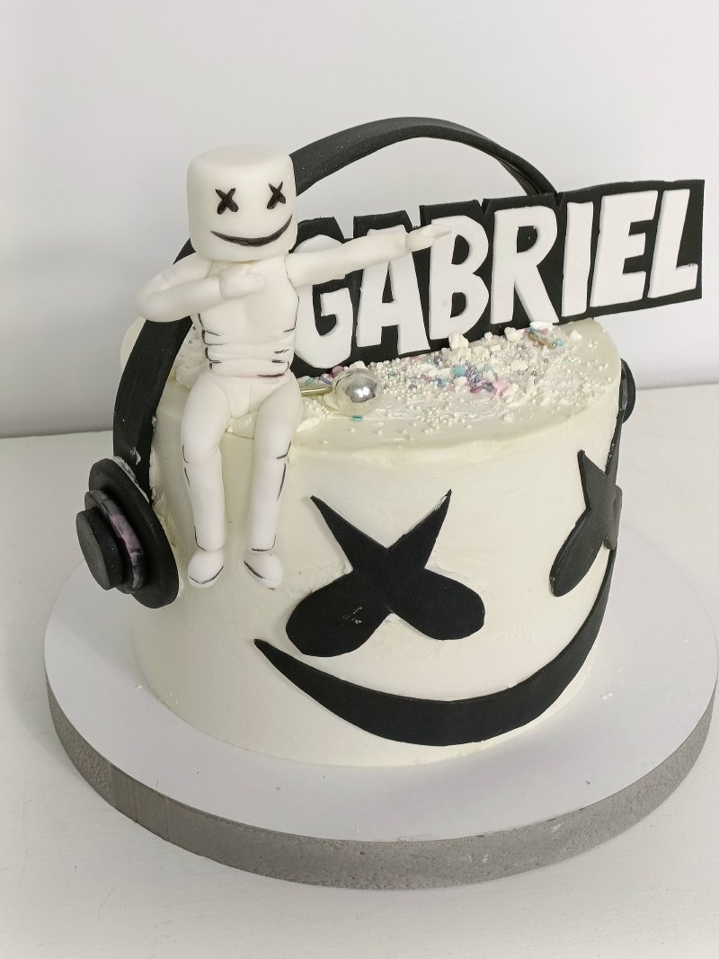 Biały tort urodzinowy z grafiką Marshmello, słuchawkami i imieniem Gabriel.
