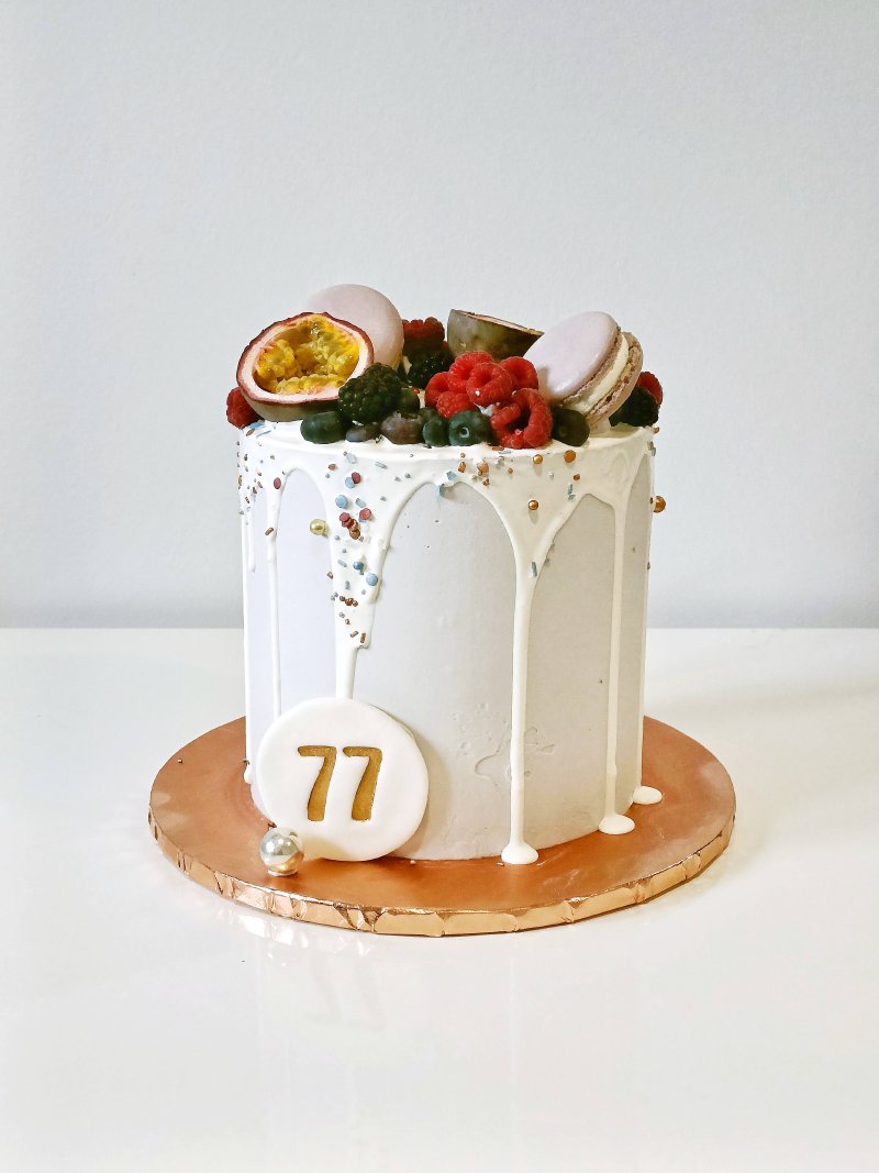 Elegancki biały tort rocznicowy ozdobiony owocami i cyfrą 77