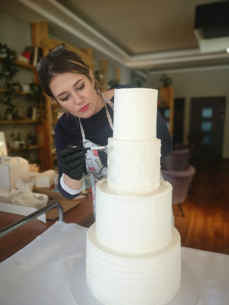 Cukiernik precyzyjnie wykańcza biały, czteropiętrowy tort weselny.